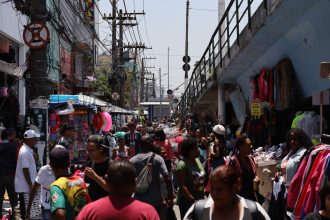Mercado de rua movimentado, com pessoas circulando entre bancas coloridas.