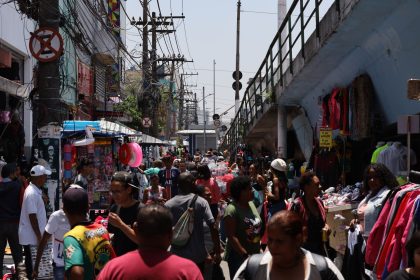 Mercado de rua movimentado, com pessoas circulando entre bancas coloridas.