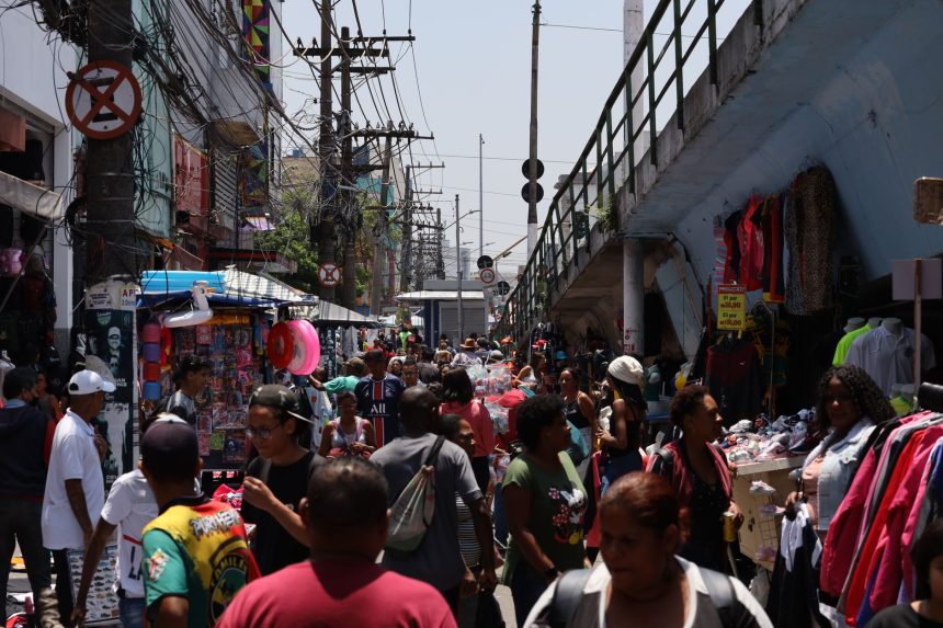 Mercado de rua movimentado, com pessoas circulando entre bancas coloridas.