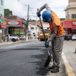 Trabalhador usando uma pá para pavimentar uma rua durante o dia.