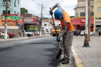 Trabalhador usando uma pá para pavimentar uma rua durante o dia.