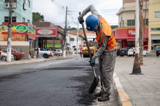 Trabalhador usando uma pá para pavimentar uma rua durante o dia.