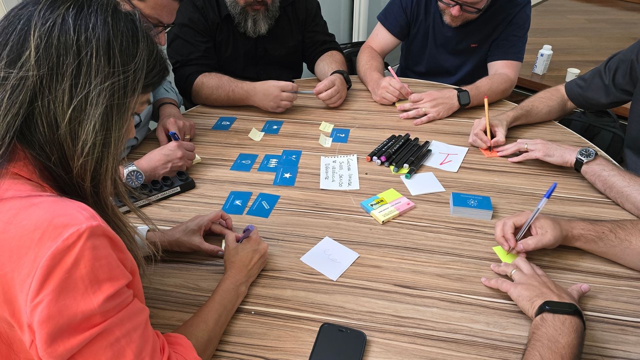 Equipe diversa participa de uma sessão de brainstorming com cartões e notas adesivas sobre uma mesa.
