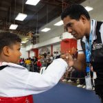 Instrutor de taekwondo parabeniza um jovem atleta durante uma competição esportiva em ambiente fechado.