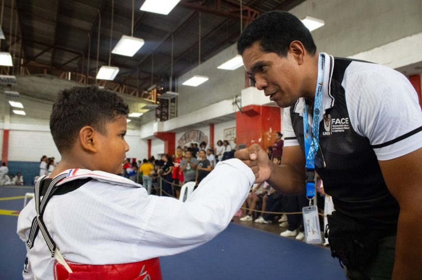 Instrutor de taekwondo parabeniza um jovem atleta durante uma competição esportiva em ambiente fechado.