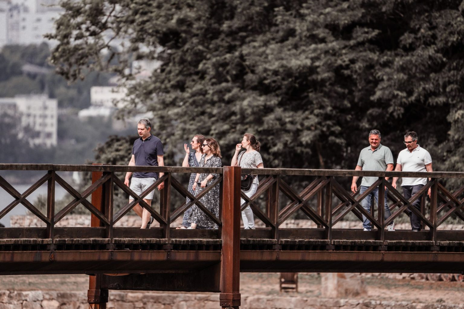 Adultos caminham por uma ponte de madeira em meio à natureza durante um passeio.