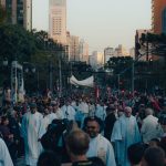 Multidão participa de uma procissão religiosa em uma região movimentada do centro de uma cidade.