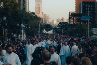 Multidão participa de uma procissão religiosa em uma região movimentada do centro de uma cidade.
