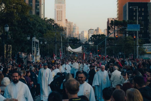 Multidão participa de uma procissão religiosa em uma região movimentada do centro de uma cidade.