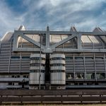 Fachada de um edifício institucional moderno, com estrutura metálica e grandes janelas.