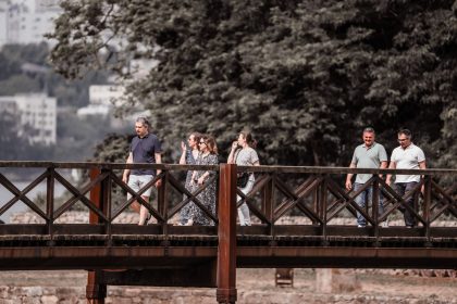 Adultos caminham por uma ponte de madeira em meio à natureza durante um passeio.